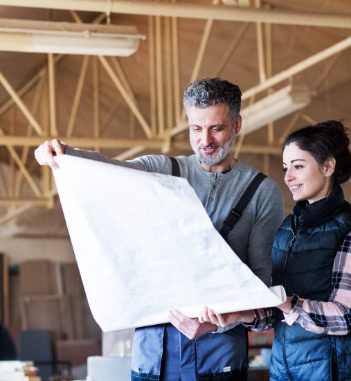 Portrait of a man and woman workers in the carpentry workshop, looking at paper plans.